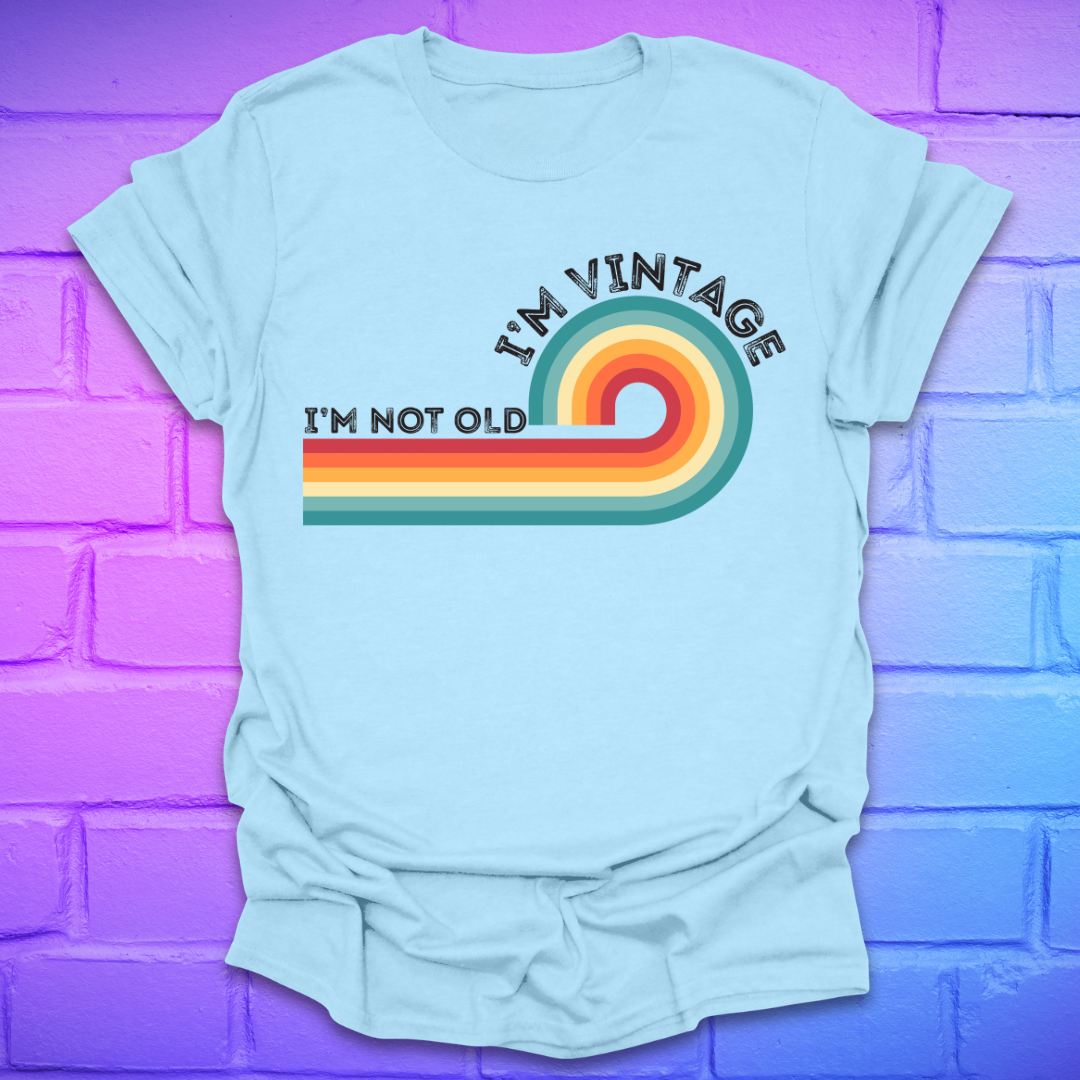 Light blue t-shirt with colorful design and text on a purple brick wall background