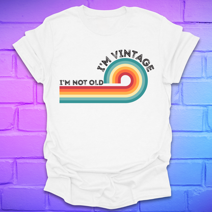 White t-shirt with 'I'm Vintage, I'm Not Old' design on a purple brick wall background