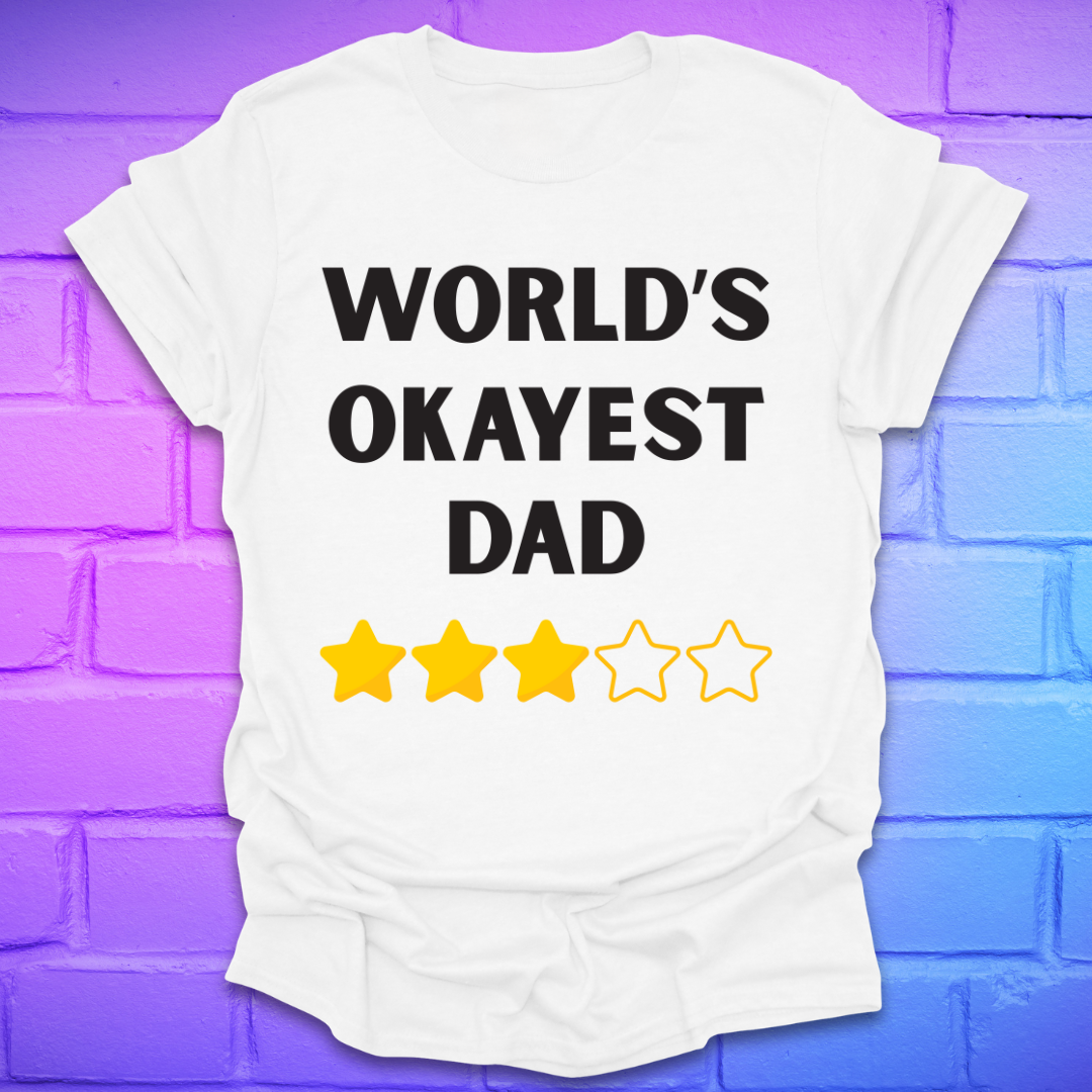 White t-shirt with 'World's Okayest Dad' text and star ratings on a purple brick wall background
