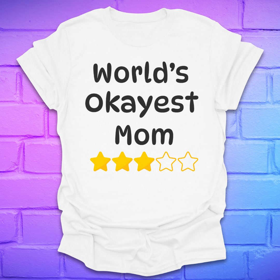 White t-shirt with 'World's Okayest Mom' text and star ratings on a purple brick wall background