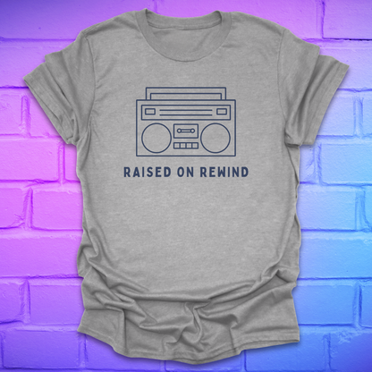 Gray t-shirt with a boombox graphic and 'Raised on Rewind' text on a brick wall background