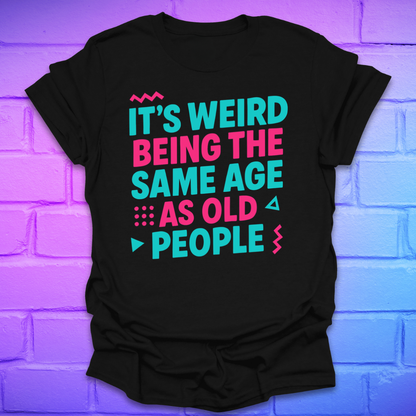 Black t-shirt with colorful text, 'it's weird being the same age as old people' on a brick wall background