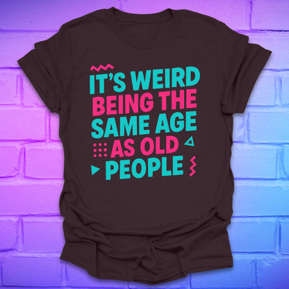 Brown t-shirt with colorful text, 'it's weird being the same age as old people' on a brick wall background