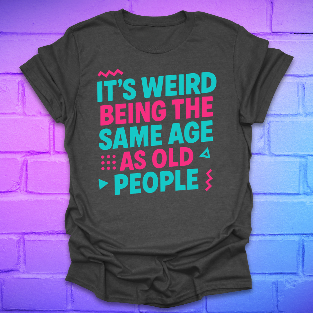 Dark grey t-shirt with colorful text, 'it's weird being the same age as old people' on a brick wall background
