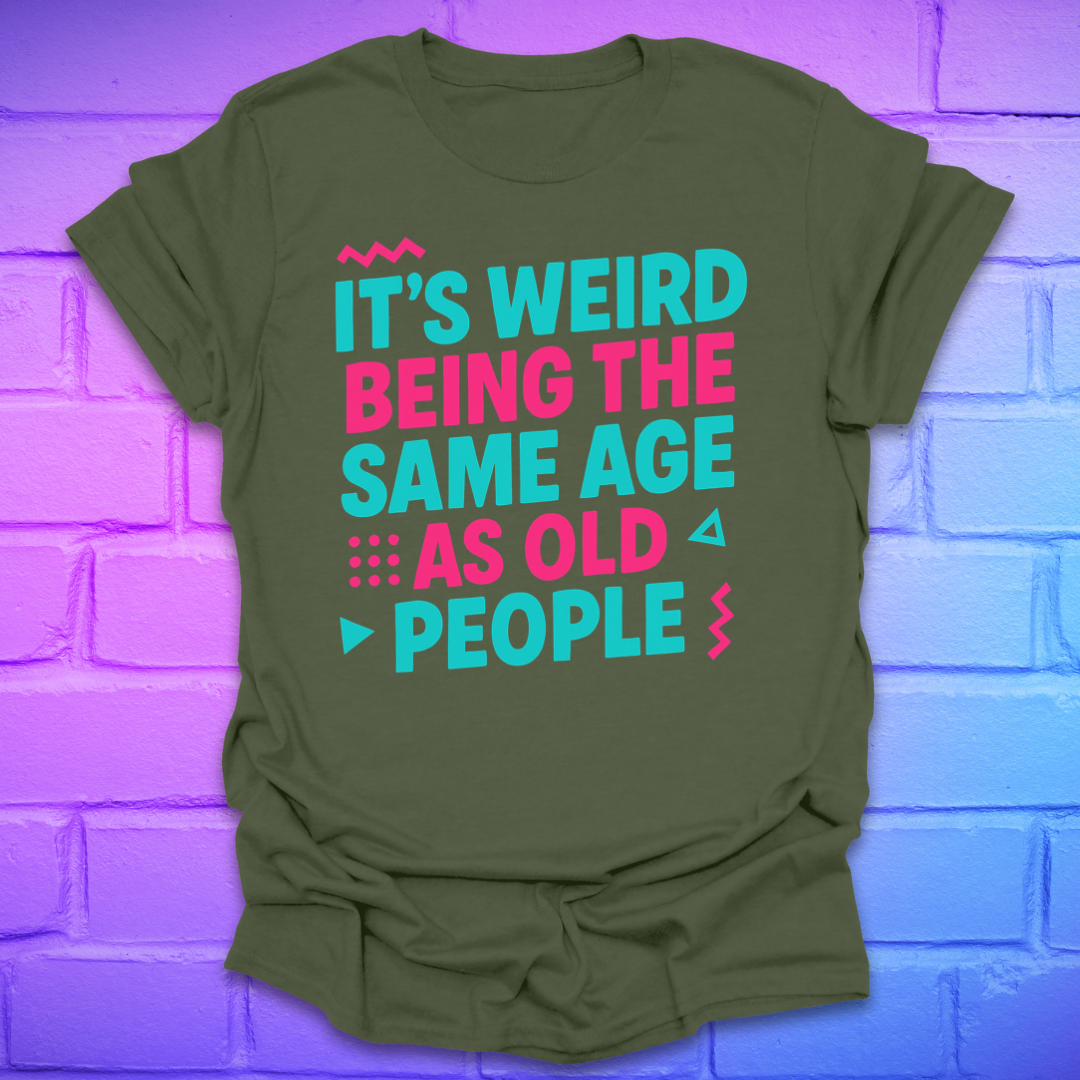 Green t-shirt with colorful text, 'it's weird being the same age as old people' on a brick wall background