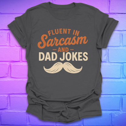 Gray t-shirt with 'Fluent in Sarcasm and Dad Jokes' text and mustache graphic on a purple brick wall background