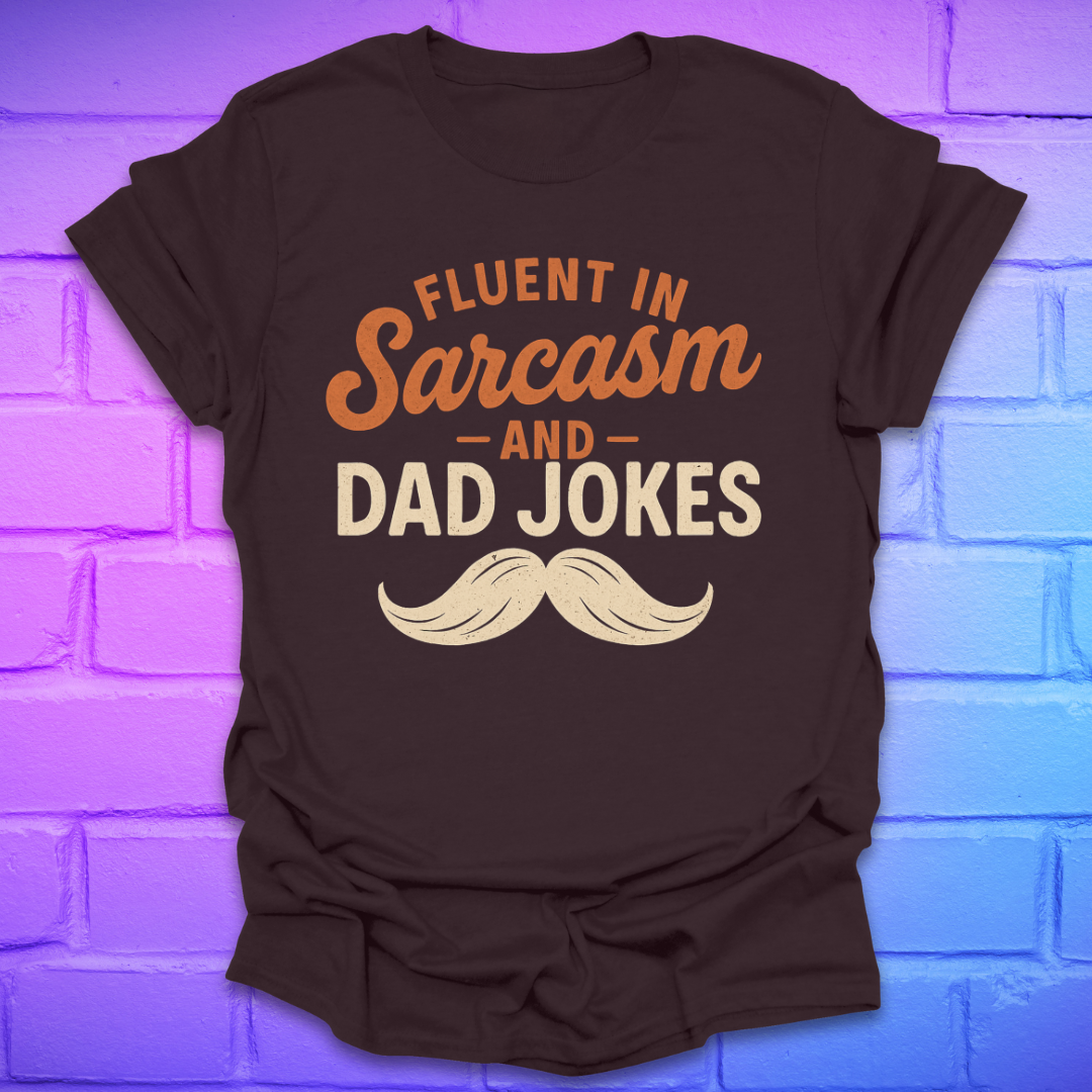 Brown t-shirt with 'Fluent in Sarcasm and Dad Jokes' text and mustache graphic on a brick wall background.