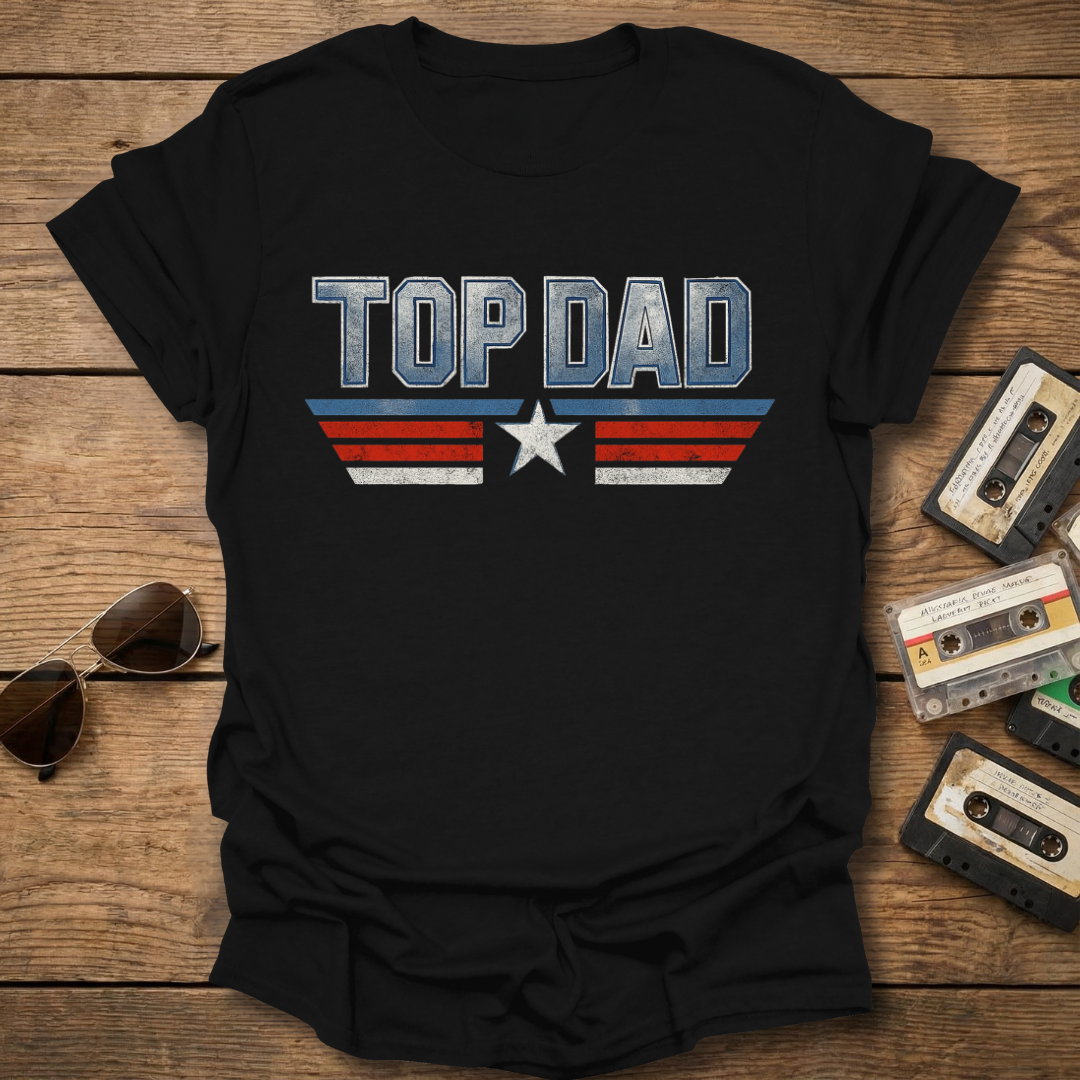 Black t-shirt with 'TOP DAD' text and star design on a wooden surface with sunglasses and cassettes.