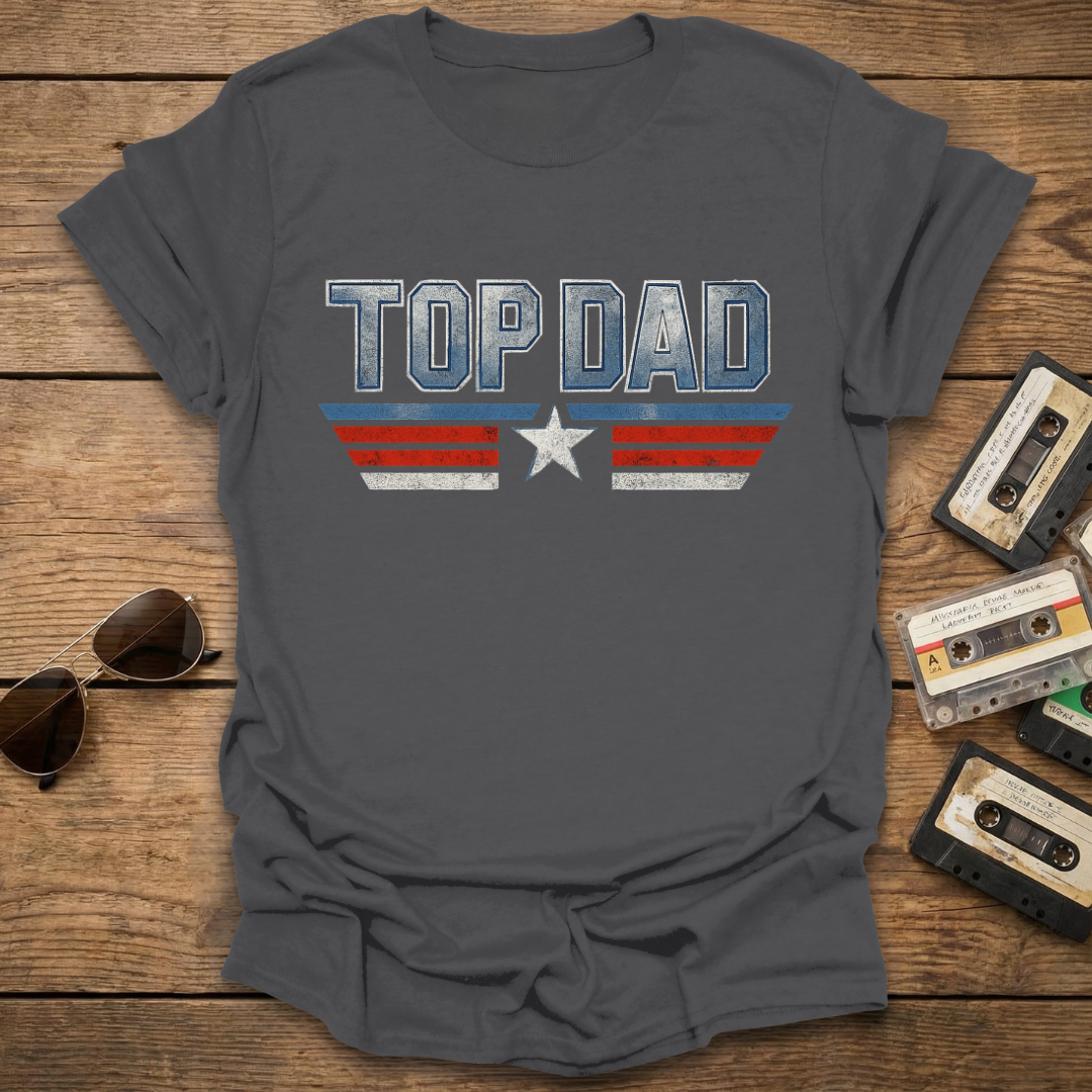 Gray t-shirt with 'TOP DAD' text on a wooden surface with sunglasses and cassettes.