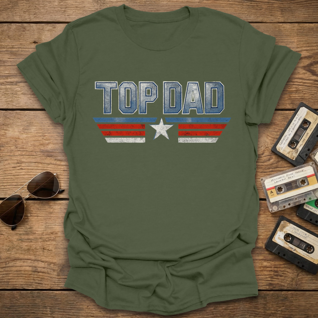 Green t-shirt with 'Top Dad' print on a wooden surface with sunglasses and cassettes.