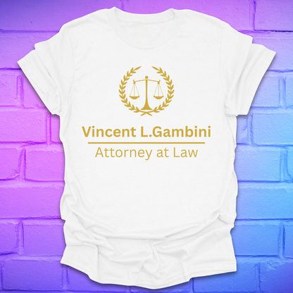 White t-shirt with 'Vincent L. Gambini Attorney at Law' text and logo on a purple brick wall background