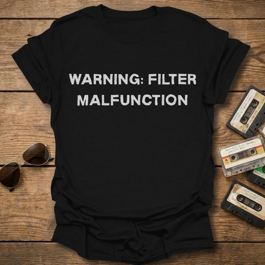 Black t-shirt with 'WARNING: FILTER MALFUNCTION' text on a wooden surface with vintage items.