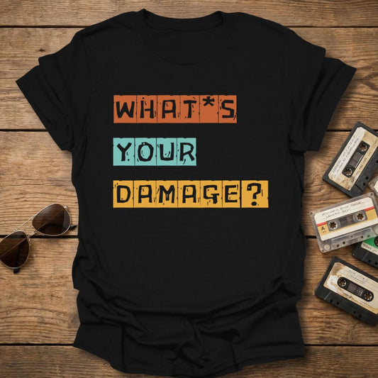 Black t-shirt with 'What's Your Damage?' text on a wooden surface with cassettes and sunglasses.