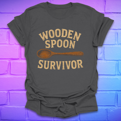 Gray t-shirt with 'Wooden Spoon Survivor' text and wooden spoon graphic on a brick wall background