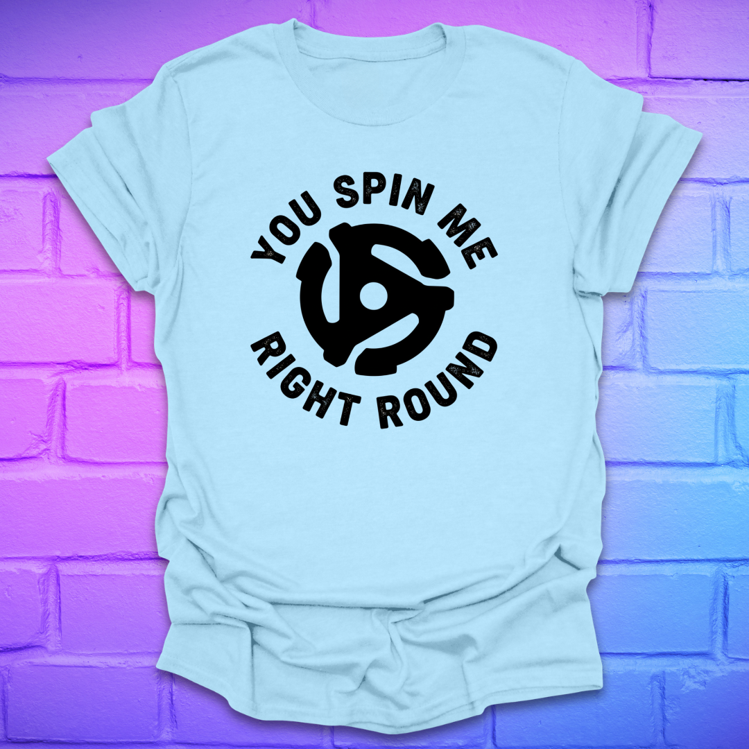 Light blue t-shirt with black graphic and text ,'you spin me right round' on a purple brick wall background