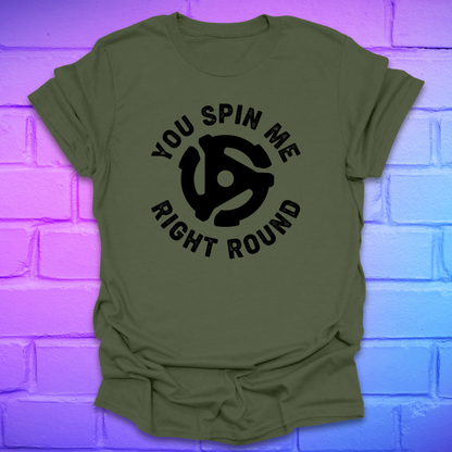 Green t-shirt with black graphic and text ,'you spin me right round' on a purple brick wall background
