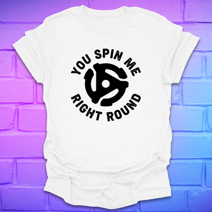 White t-shirt with black graphic and text ,'you spin me right round' on a purple brick wall background